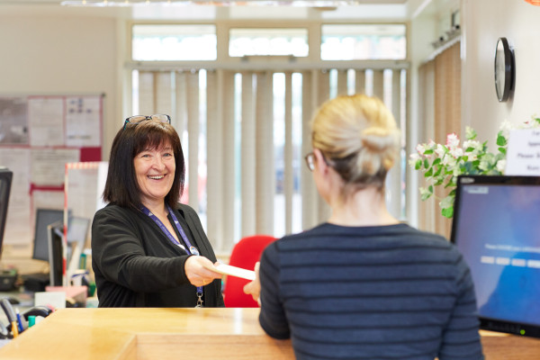 A photo showing a receptionist giving a patient a prescription at Rawcliffe surgery
